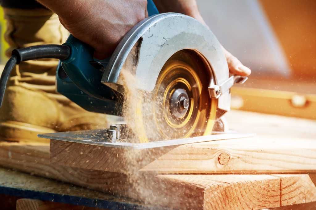 carpenter building contractor using hand held circular saw to cut boards constructiion project