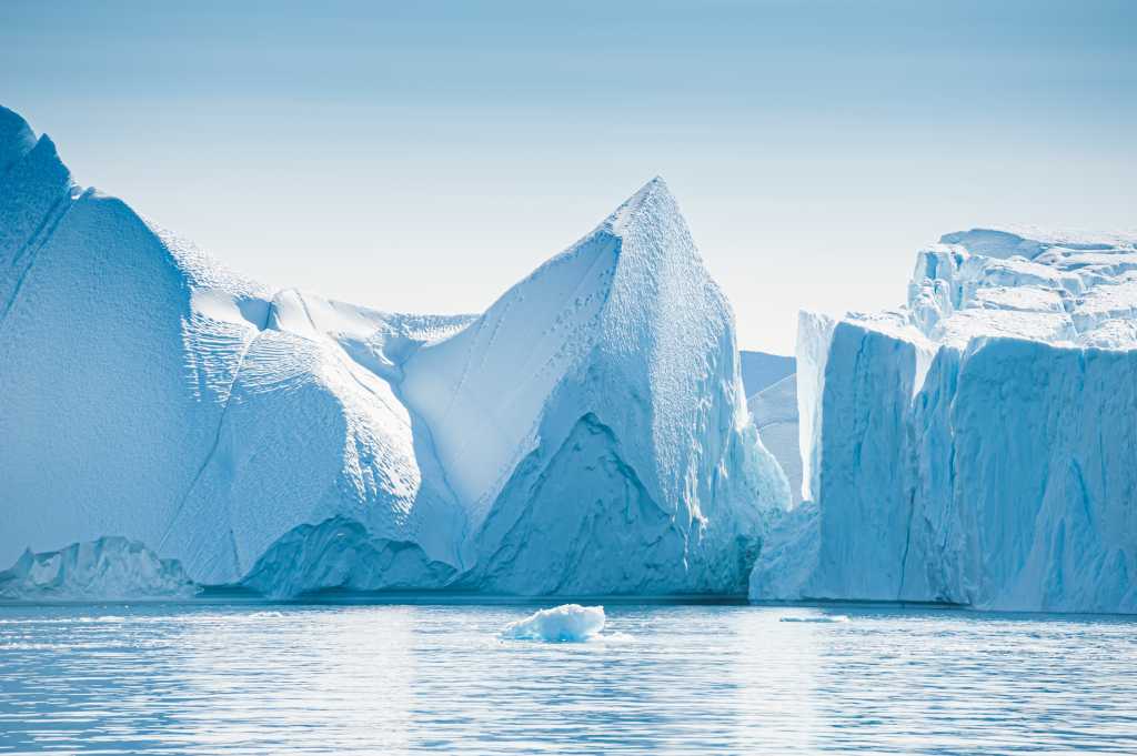 Big icebergs in Atlantic ocean, Ilulissat icefjord, western Greenland. Blue sea and the blue sky at sunrise