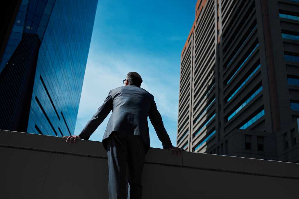 Business, man and thinking at city on rooftop about career or future with goal in company. Professional, person and skyscraper on roof is standing with vision or hope for decision as leader at work.