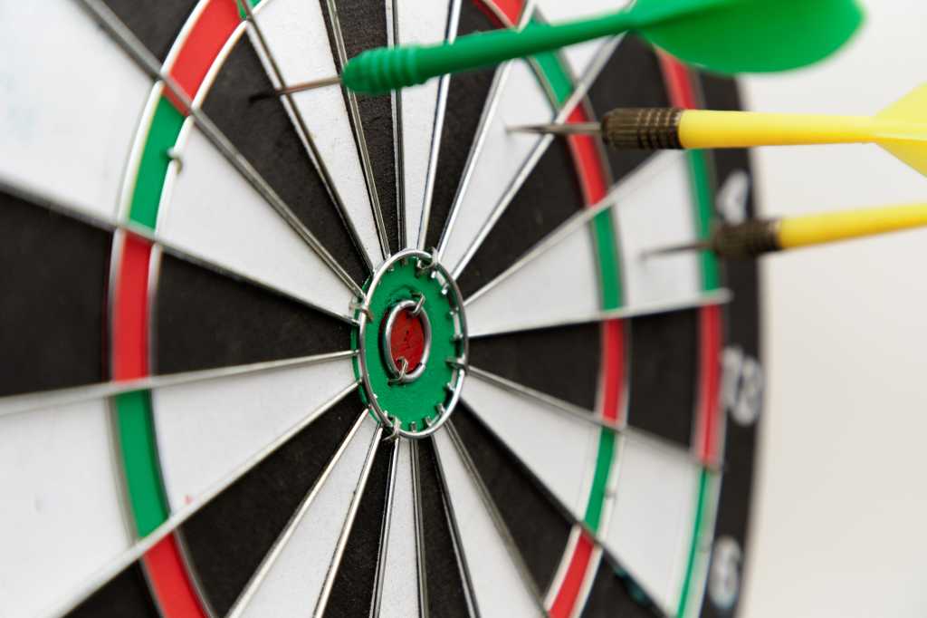 Missed target, missed bullseye. Classic dartboard with green and yellow darts wide of the mark.