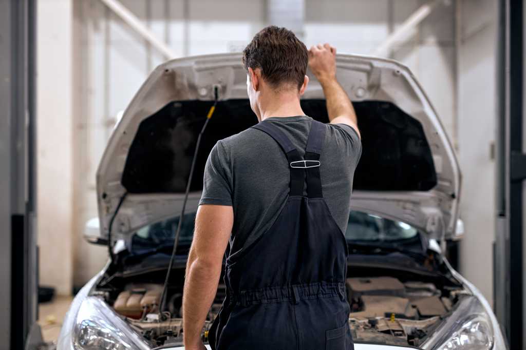 A person stands looking under the hood of a car.