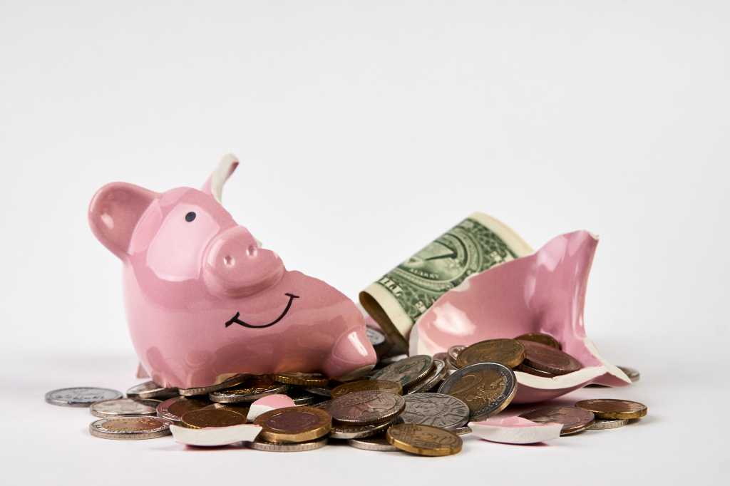 Broken piggy bank with coins money spilled against a white background, close-up