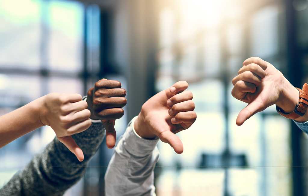 four hands raised with thumbs down in front of window with blurred light