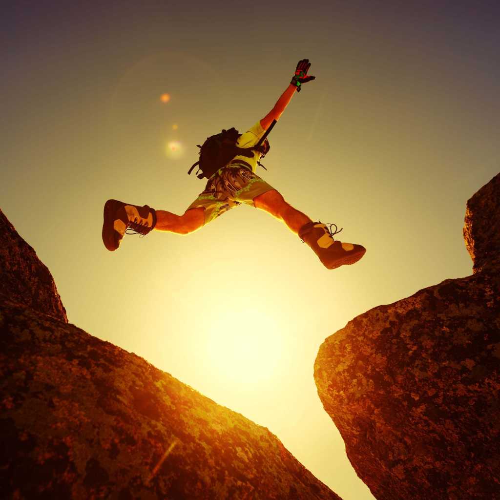 Leap, jump, risk, adventure. A person leaping between two boulders.