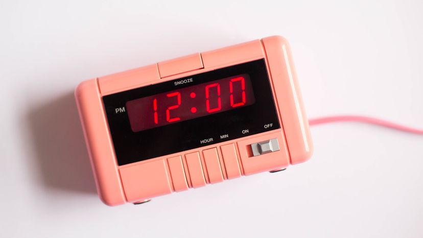 Pink alarm clock on white background displaying 12 PM